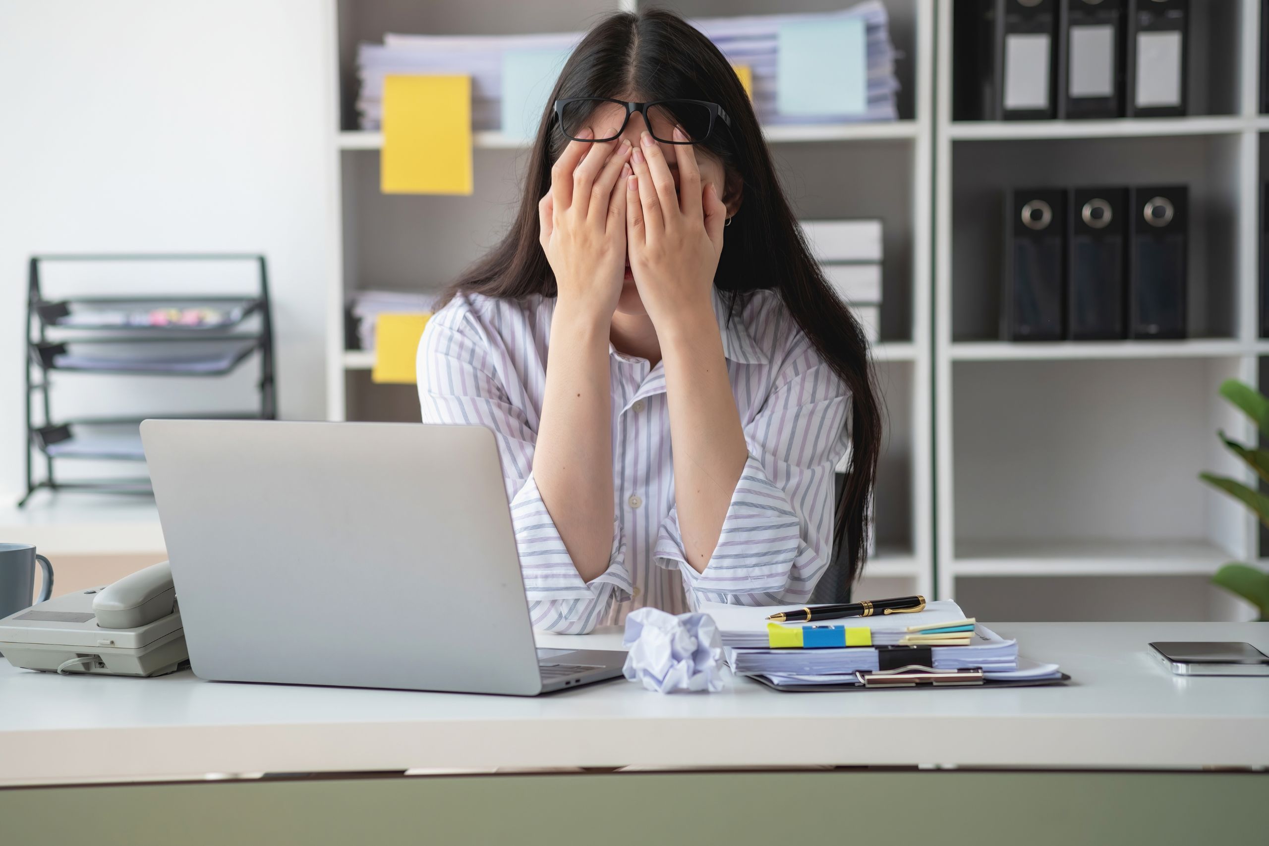 woman at work sitting at her desk with her head in her hands struggling with high functioning depression symptoms