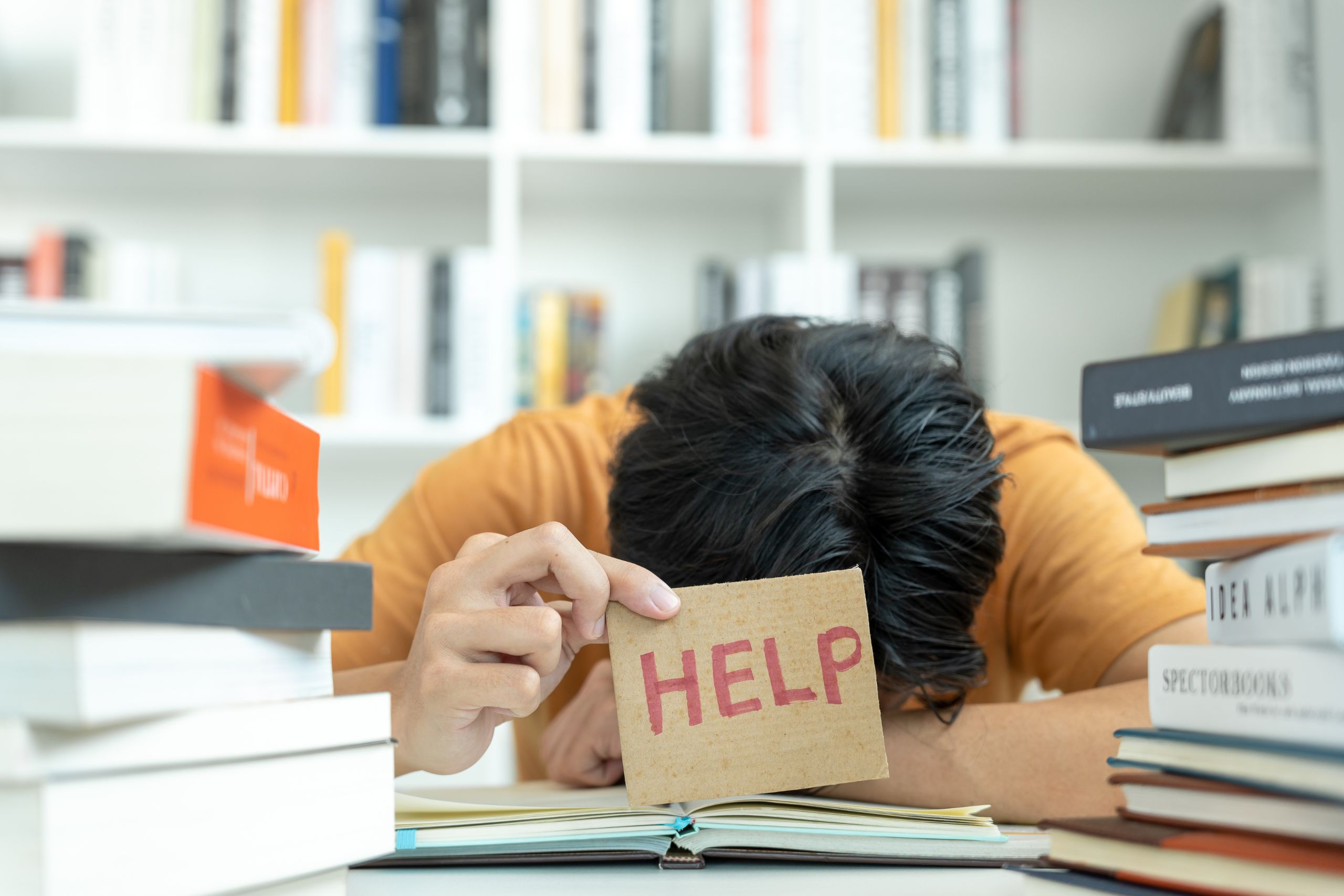 woman with her head on her work desk holding a sign that says help because she doesnt know how to cope with high functioning anxiety